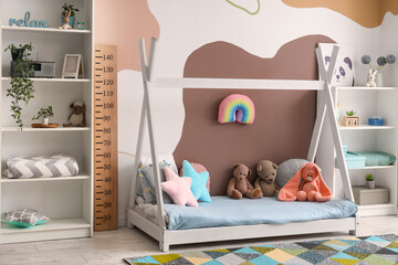 Stylish children's bedroom interior with cozy bed, toys and wooden stadiometer
