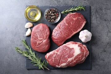 Raw beef steaks, oil and spices on grey background, top view