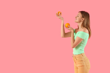 Pretty young woman with oranges on pink background