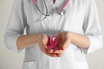 Mammologist with pink ribbon on light background, closeup. Breast cancer awareness