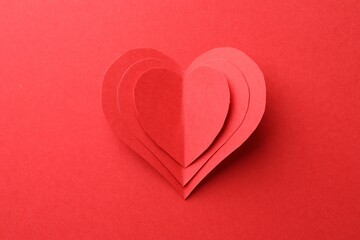 Paper hearts on red background, top view