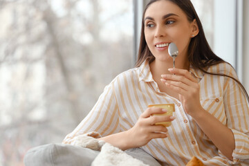 Thoughtful young woman with tasty yoghurt at home, closeup