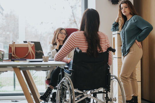 Diverse workplace featuring a wheelchair-using woman engaging in a discussion with colleagues in a modern office setting.