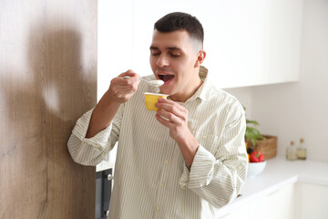 Fototapeta premium Young man eating tasty yogurt in kitchen