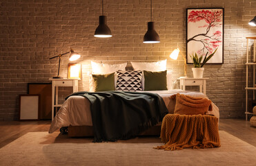 Interior of modern bedroom with blankets on comfortable bed and glowing lamps at night
