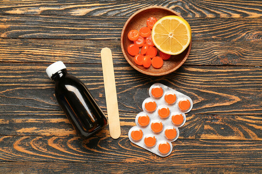 Pills for sore throat with cough syrup, tongue depressor and lemon on wooden background