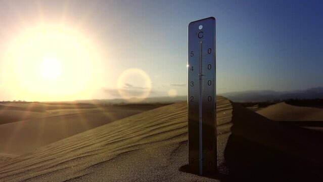 Wind blows over a dune ridge where a thermometer is stuck against the sun in the background
