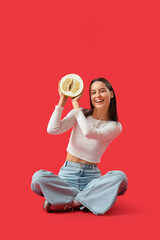 Smiling young woman with half of pomelo sitting on red background