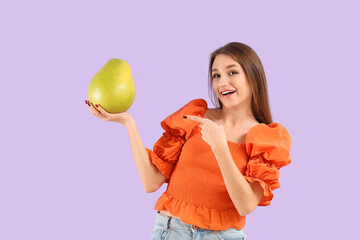Smiling young woman pointing at pomelo on lilac background