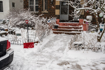 Snow on a recently cleared  older residential street sidewalk with parked cars and a red bladed snow shovel shot in beaches neighbourhood toronto