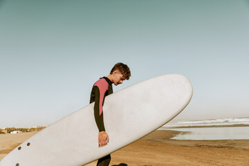 Back view of male surfer in wetsuit with his surfboard entering the sea. Surfing and ocean