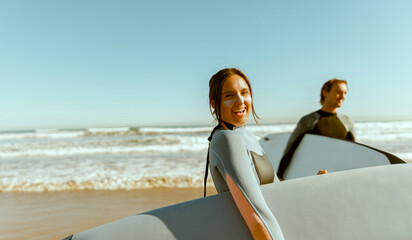 Smiling surfers with surfboards in wetsuit are walking on the beach after ride the waves