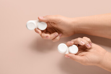 Female hand with containers for contact lenses on beige background