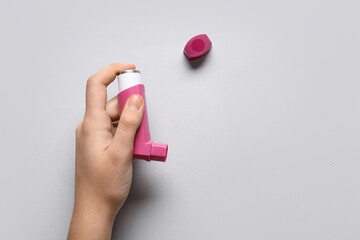 Child's hand with asthma inhaler on white background