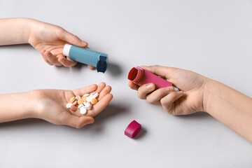 Child's hands with asthma inhalers and pills on white background
