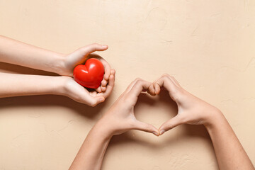 Hands of woman and child showing heart gesture and holding decoration on beige background