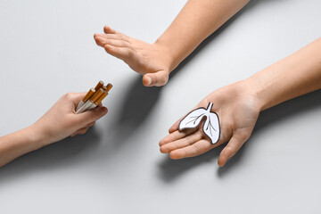 Female hands with paper lungs rejecting cigarettes on grey background