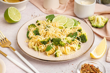 Delicious fusilli pasta with broccoli, cheese and lime slices in plate on light background, closeup