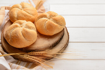 Board with delicious kaiser rolls and wheat ears on white wooden background, closeup