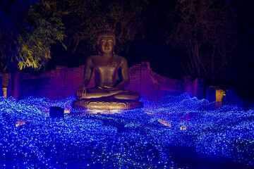 A gold Buddha statue in a debris ancient temple with blue LED light set on ground