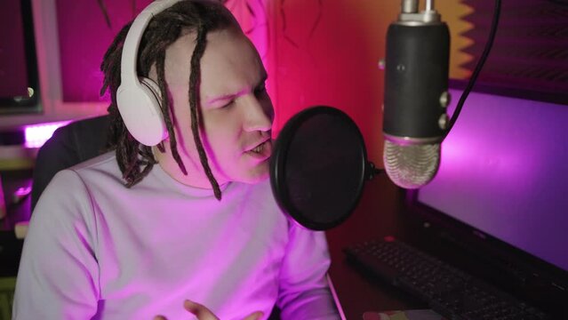 A young male rapper is recording his hip-hop song in a home studio, a man with dreadlocks is raping into a microphone while sitting in front of a computer