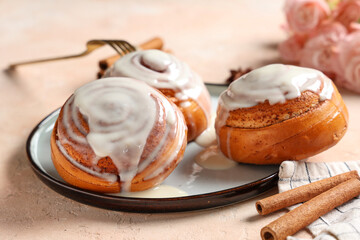 Plate with glazed buns and cinnamon sticks on beige grunge background