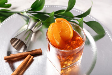 Metal plate with glass of delicious Old Fashioned Cocktail, orange slices and cinnamon sticks on...