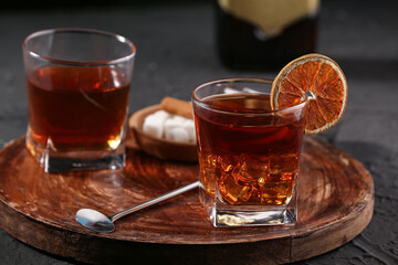 Wooden board with glasses of delicious Old Fashioned Cocktail and orange slice on black grunge background
