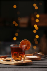 Board with glass of delicious Old Fashioned Cocktail and orange slice on black wooden table