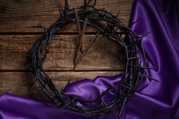 Crown of thorns with purple fabric and nails on wooden background