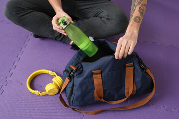 Young man putting bottle of water into sports bag  in gym