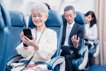 飛行機でスマホを使うシニア女性