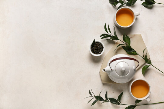 Teapot with cups, bowl of dry tea and leaves on white grunge background