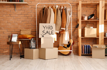 Cardboard with text YARD SALE and various unwanted things near brick wall in room