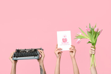 Hands holding vintage typewriter, tulips and festive postcard with text 8 MARCH HAPPY WOMEN'S DAY on pink background