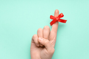 Female hand with red bow on index finger against turquoise background. Reminder concept