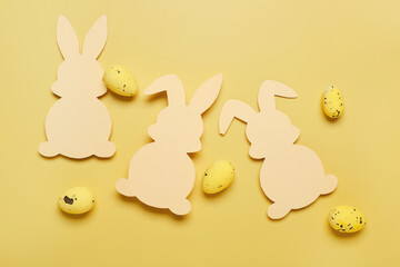 Paper bunnies with Easter eggs on yellow background