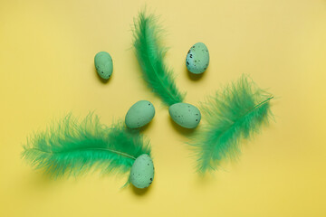 Fototapeta na wymiar Green Easter eggs with feathers on yellow background