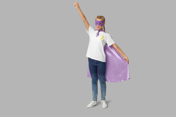 Cute teenage girl in superhero costume with yellow ribbon on grey background. International Childhood Cancer Day
