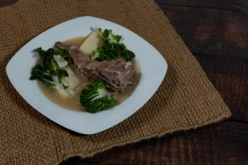 Traditional Filipino pork sinigang with bok choy in a white bowl on a table mat.
