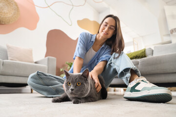 Young woman with cute British Shorthair cat sitting on floor at home