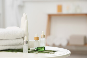 Fototapeta na wymiar Cosmetic dropper bottles with palm leaf and towels on table in bathroom, closeup