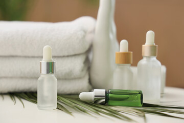 Cosmetic dropper bottles with palm leaf and towels on table in bathroom, closeup