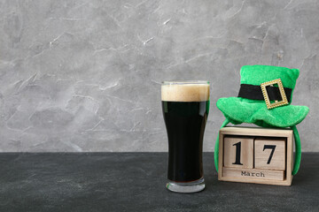 Glass of dark beer with leprechaun hat and calendar for St. Patrick's Day celebration on black...