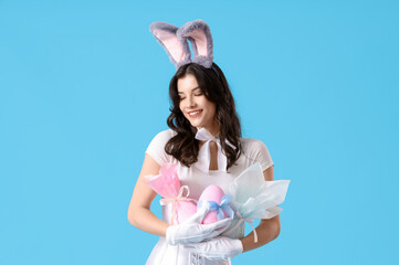 Sexy young woman in bunny costume with Easter gift eggs on blue background