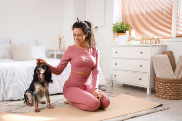 Sporty young African-American woman with cocker spaniel sitting in bedroom