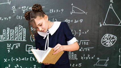 Girl reading a book standing blackboard, homework report in front of the school class.