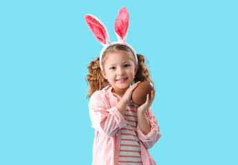 Cute little girl in bunny ears with chocolate Easter egg on blue background - obrazy, fototapety, plakaty