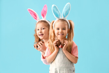Obraz na płótnie Canvas Cute little girls in bunny ears with chocolate Easter eggs on blue background