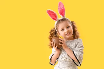 Poster Im Rahmen Cute little girl in bunny ears with chocolate Easter egg on yellow background © Pixel-Shot